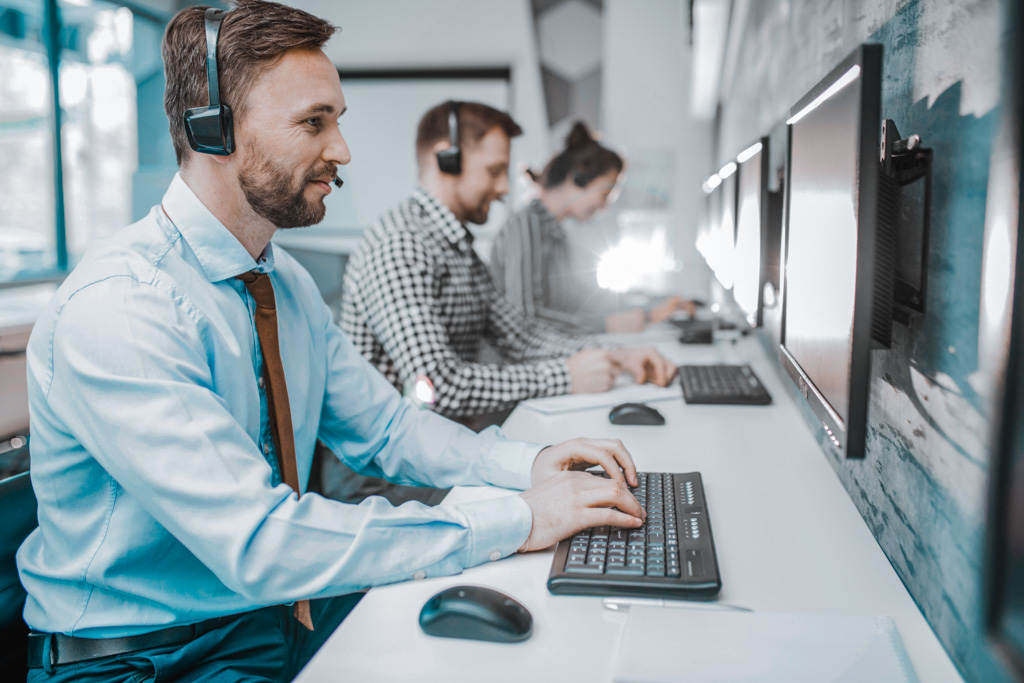 Side view portrait of handsome bearded man wearing headset working with group of help desk operators sitting in row, copy space